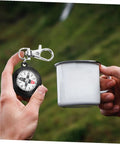 Person holding Compact Hiking Compass Keychain With Snap Hook Lightweight Plastic Pocket Compass during outdoor camping
