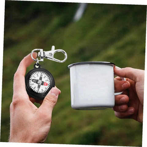 Person holding Compact Hiking Compass Keychain With Snap Hook Lightweight Plastic Pocket Compass during outdoor camping