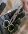 Gloved hand holding 5.25 inch Workhorse Pro Grade Stainless Steel Electrician Scissors with free-fall handle and serrated blades