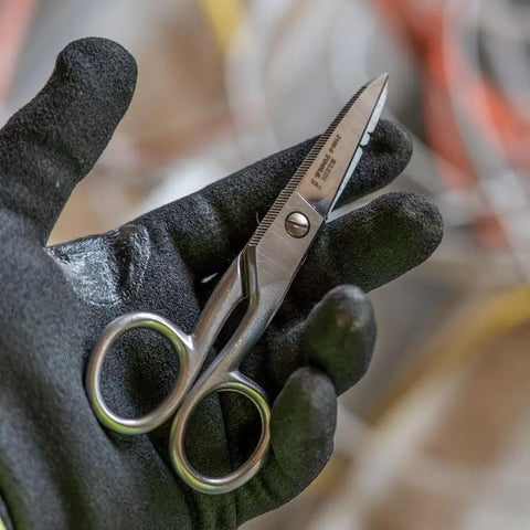 Gloved hand holding 5.25 inch Workhorse Pro Grade Stainless Steel Electrician Scissors with free-fall handle and serrated blades