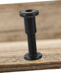 Kickass Black Stainless Steel M6 X25 Chicago Screw showing threaded design on wood surface for leather crafting and bookbinding.