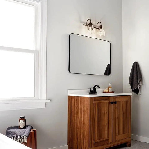Avery 14.75 Inch Two-Light Vanity Light With Clear Seeded Glass In Olde Bronze over bathroom mirror and wooden vanity cabinet.