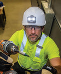 Worker wearing vented safety helmet with rechargeable headlamp for at height and confined space work, lightweight hard hat with secure mounts.