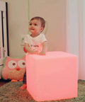 Child next to Rechargeable 12 Inch LED Light Cube Stool With Remote Control Mood Lamp, glowing pink in nursery