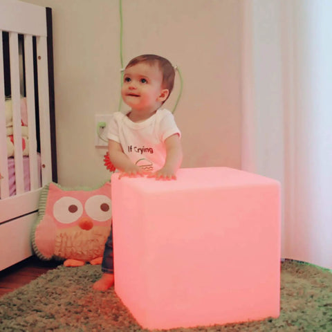 Child next to Rechargeable 12 Inch LED Light Cube Stool With Remote Control Mood Lamp, glowing pink in nursery