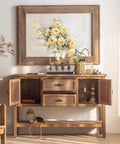 Wooden cabinet with open doors, decorative handles, and a floral painting above; a basket and candles resting on top.