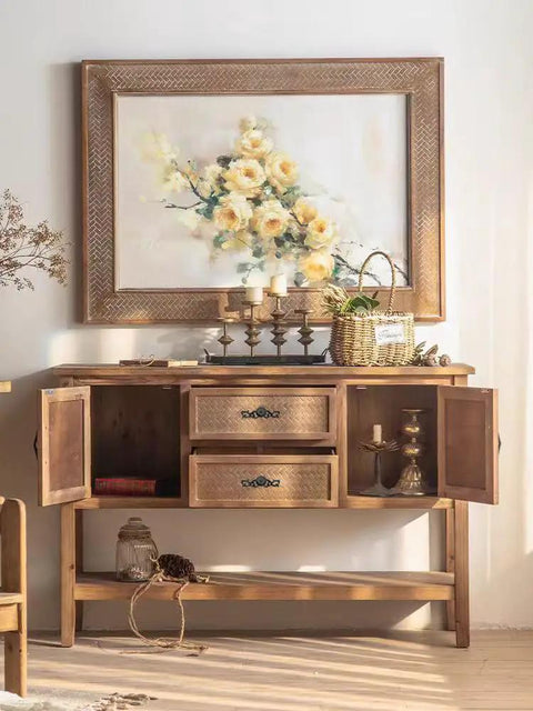 Wooden sideboard with open cabinet doors under a framed floral painting and candle holders
