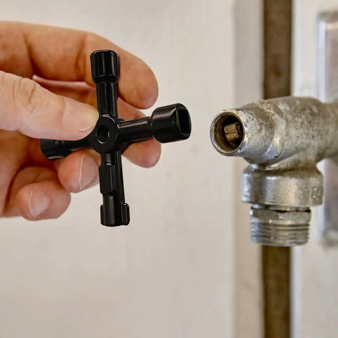 Hand holding 4-Way Universal Utility Cabinet Key 2 Pack In Black For Gas Meters, Water Panels, And Electric Boxes near a valve