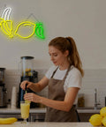 Woman making smoothie under Bright Dope Banana Shaped LED Neon Sign Light For Bedroom Decor, Kids Room Wall Art, Party Bar Glow, lemon art.
