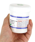 Hand holding a jar of RMA 218 Flux Paste For BGA Reballing And Soldering, 100g size, white container.