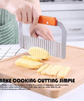 Side view of stainless steel wavy crinkle cutter with wooden handle cutting potato on a wooden board