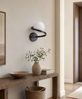MAHGNTKCX Black Wall Sconce with Opal Glass Globe and Spiral Metal Frame above a wooden console with decor.