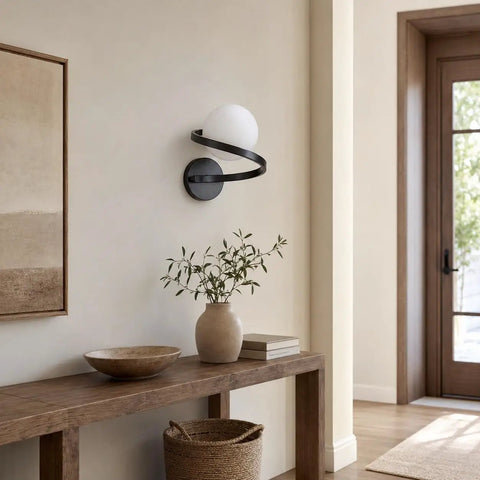MAHGNTKCX Black Wall Sconce with Opal Glass Globe and Spiral Metal Frame above a wooden console with decor.