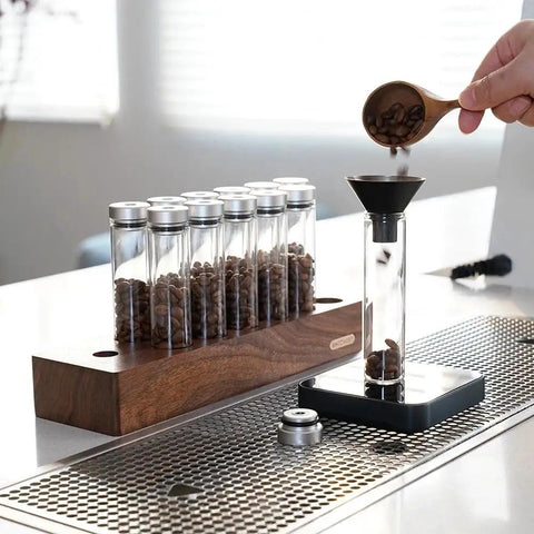 12 Piece Single Dose Coffee Bean Storage Tubes With One Way Exhaust Valve Glass Vials On Sturdy Walnut Wood Base and Easy Pouring Funnel in use.