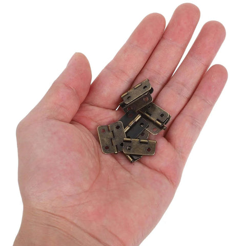 Person holding 1:12 Scale Miniature Bronze Hinges Set Of 20 With 80 Screws For Dollhouse Furniture Cabinet Closet DIY Projects Antique Brass Finish