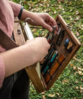 Person using Wooden Messenger Box Crossbody Bag For Artists Grab And Go Multifunctional Handmade Tool Storage Box Painting Brush Organizer Sketch Box And Portable Easel Case For Outdoor Painting Brown