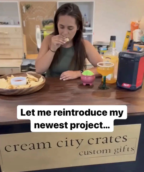 A woman tasting chips at a wooden counter with snacks and drinks, promoting Cream City Crates custom gifts.