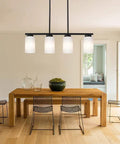 Farmhouse Four Light Pendant Island Light in black finish with opal white glass shades over dining table in minimalist kitchen