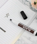 Scratch Fix Marker Pen For Wood Floors And Furniture, black, shown on notebook with cap off, with star doodle.