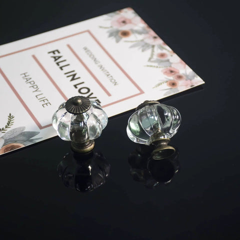 Two clear acrylic pumpkin cabinet knobs next to a floral card, decorative drawer pull handles, vintage style.