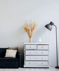 Modern living room with black sofa, gray dresser, tall black floor lamp, and dried pampas grass arrangement.