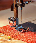 Close-up of a silver snap-on presser foot on a domestic sewing machine with red fabric underneath (zigzag/straight stitch)