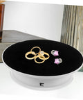 Rotating Electric Turntable Display Stand With Smooth Motorized Motion showcasing gold rings and earrings on a black surface.