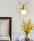 Brass Antlers Wall Sconce With E27 Socket Creates A Cozy Top Tier Glow For Bedrooms And Living Rooms Featuring Easy Peasy Install Vibes That Make It A Stunning Head Turner For Any Space, mounted above bedside decor.