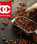 Silver scoop with coffee beans on a dark surface near a burlap sack, with a red 'bene casa' logo in the corner.