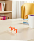 Single orange glider from Five Pack Rubber Band Powered Glider Plane Kit For Kids And Fam on a desk.