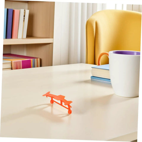 Single orange glider from Five Pack Rubber Band Powered Glider Plane Kit For Kids And Fam on a desk.