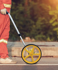 Person using Beefy Rolling Measuring Wheel Straight From The Box For Long Distance Tracking With Five Digit Mechanical Counter on a path.
