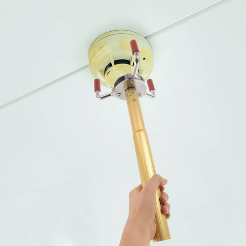A hand holding a lightweight aluminum smoke transducer removal tool reaching towards a ceiling smoke detector.