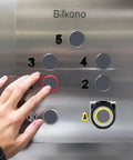 Person pressing elevator button with Eight Piece Push Button Cover Set Keeps You From Accidentally Pressing Buttons On Elevators Washing Machines And Office Equipment With Dustproof Waterproof Plastic Protection visible.