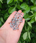 Hand holding 316 Stainless Steel D Shackle Mini Shackles For Paracord Jewelry And Bracelet Hardware Built Tough Marine Grade Rigging 1 Eighth Inch Pin Opening Durable Pack Of 10 For Survival Gear And Craft Projects against a leafy background