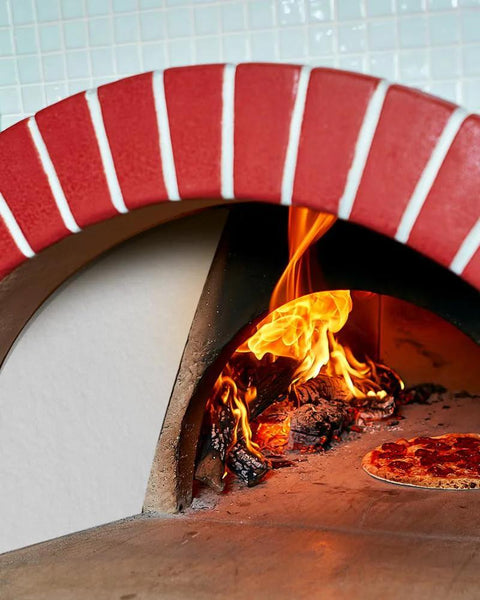 Pizza cooking in a red-brick wood-fired oven with visible flames inside