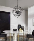Cubist Pendant Metron Chandelier in black with interlocking open cube frame hangs above a white dining table with black chairs.