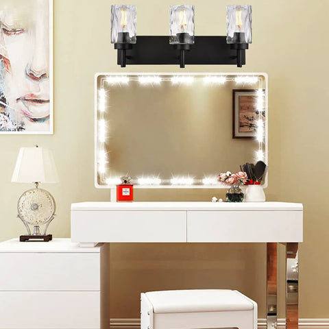 Three Light Modern Vanity Wall Sconce In Black With Hammered Glass Shades above illuminated mirror in dressing table setup