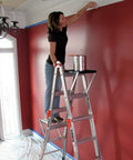 Heavy Duty Project Tray Organizer with Paint Container Slots on ladder used by person painting red wall in room, 25 lb load