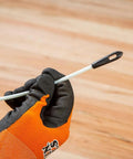 Close-up of white Klein Tools non-conductive fish tape end with black tip, held by an orange-gloved hand.