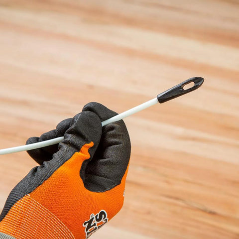 Close-up of white Klein Tools non-conductive fish tape end with black tip, held by an orange-gloved hand.