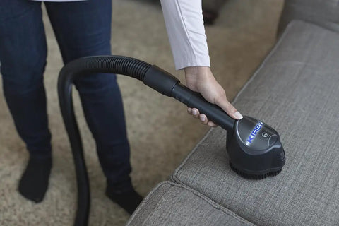 Person using vacuum on gray couch for cleaning upholstery