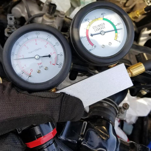 Automotive cylinder leak-down tester kit with dual gauges and extension rod, front view on engine.