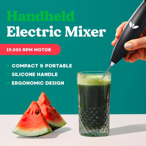 Person using all in one handheld milk frother and drink stirrer for coffee, matcha, greens, protein shakes stainless steel battery operated wand that whips up creamy foam fast beside watermelon slices