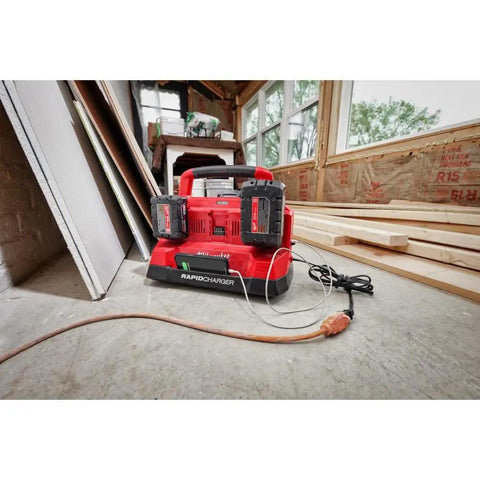 Six Bay M18 Rapid Charger For Batteries on a construction site floor, charging two batteries simultaneously, USB cable attached.