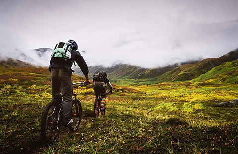 Two cyclists riding on a mountain trail, showcasing the use of Two Pack 26 Inch Bike Inner Tubes With Schrader Valve 33mm Durable Butyl Rubber.