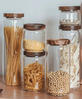 Top Shelf Airtight Glass Storage Jars With Smooth Acacia Wood Lids filled with pasta, grains, and spices on a wooden surface.