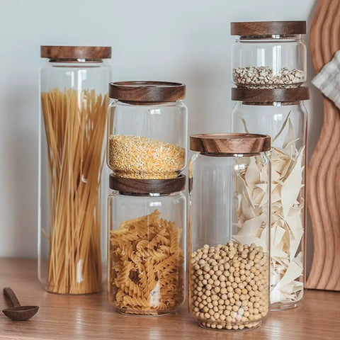 Top Shelf Airtight Glass Storage Jars With Smooth Acacia Wood Lids filled with pasta, grains, and spices on a wooden surface.