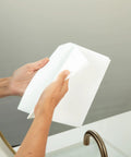 Spiff cleaning cloth, white, held by hands near bathroom sink and mirror