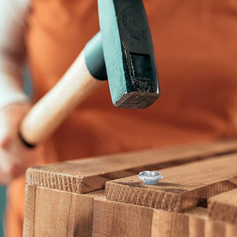 Close-up of a 3/8-16 zinc-plated steel T-nut on wood with hammer overhead.